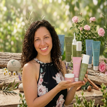 Bianca Wild präsentiert lächelnd die hochwertigen Naturprodukte von Relight Delight vor einer idyllischen, natürlichen Kulisse aus Holz und Blumen.